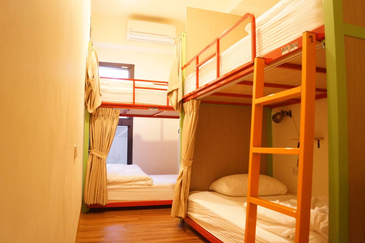 A dormitory room with bunk beds, a window with curtains, and an air conditioning unit.