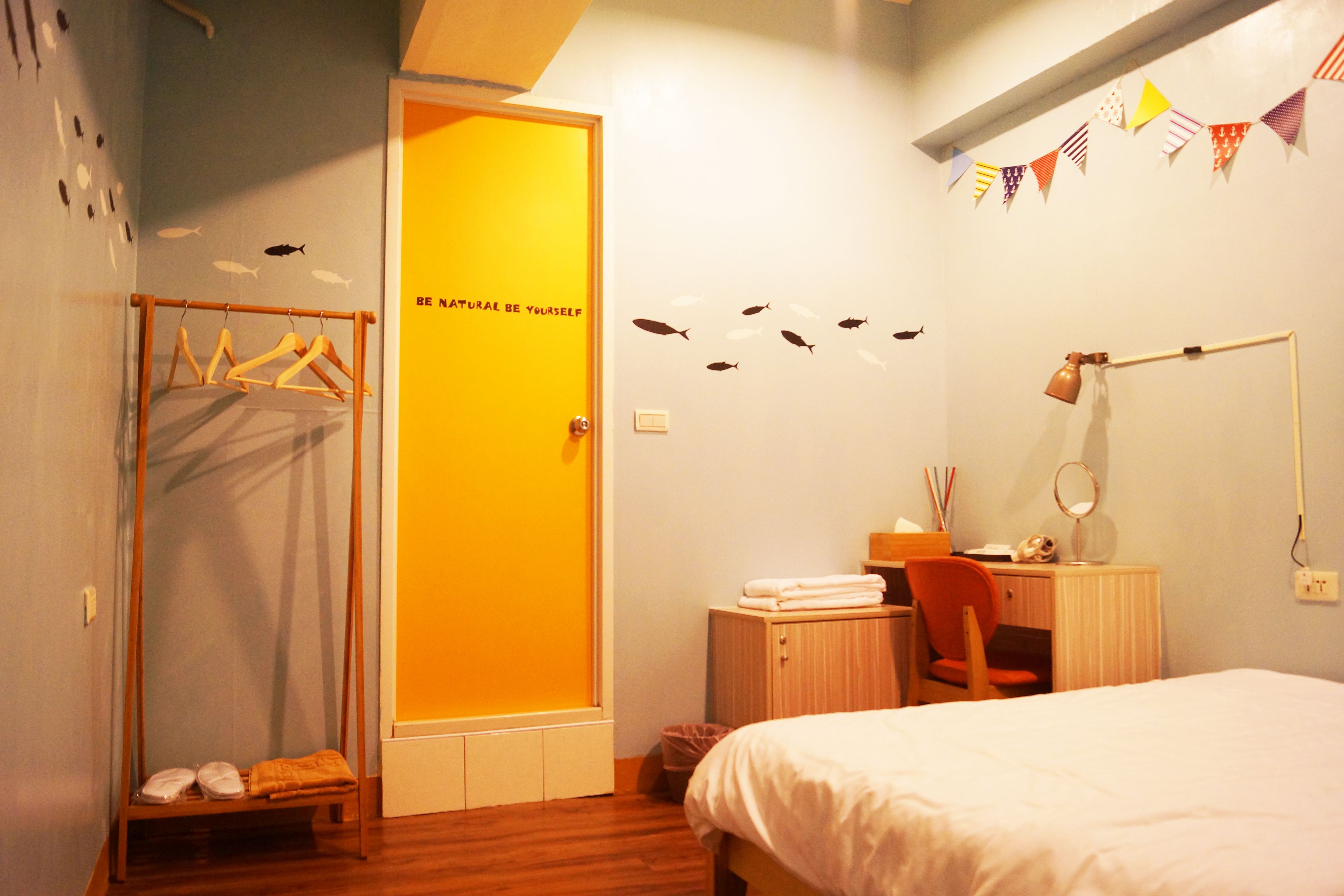 A bedroom with a bed, a desk with a chair, a wardrobe, and a door with a motivational quote.