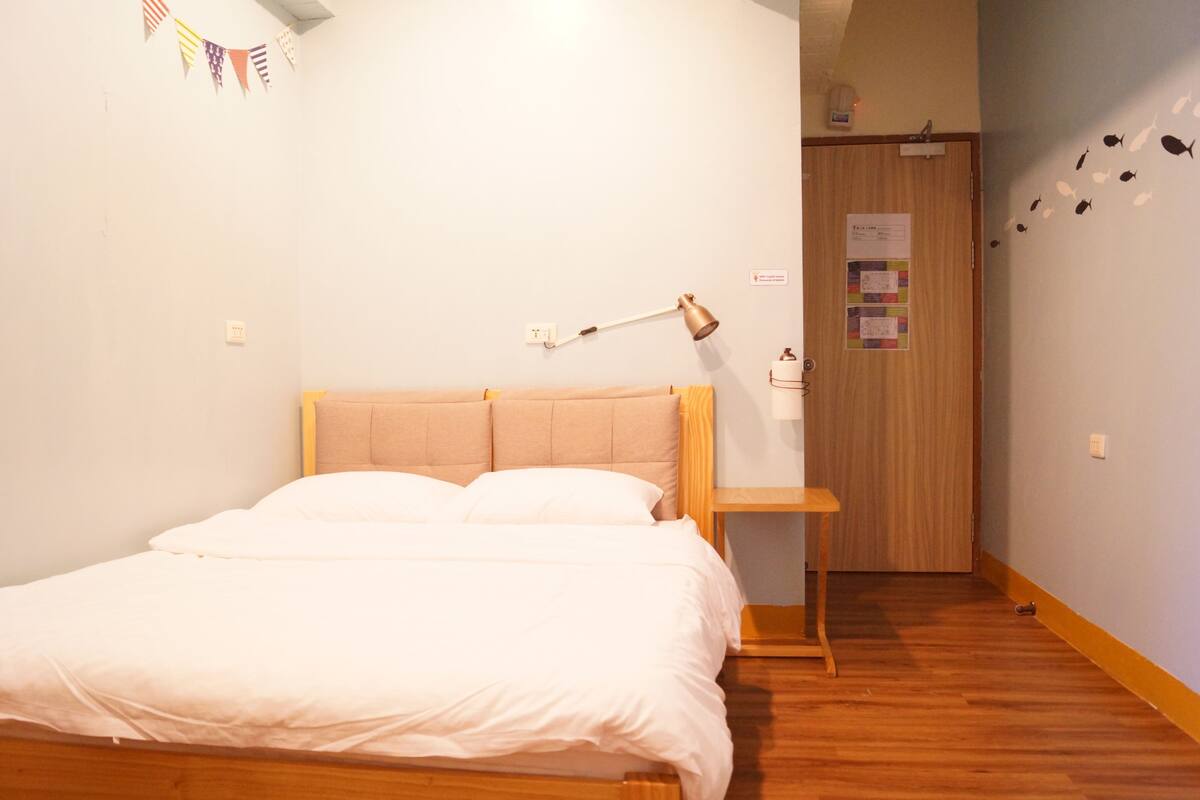 A bedroom with a wooden bed, a bedside table with a lamp, a wooden door, and a wall with a fish decal.