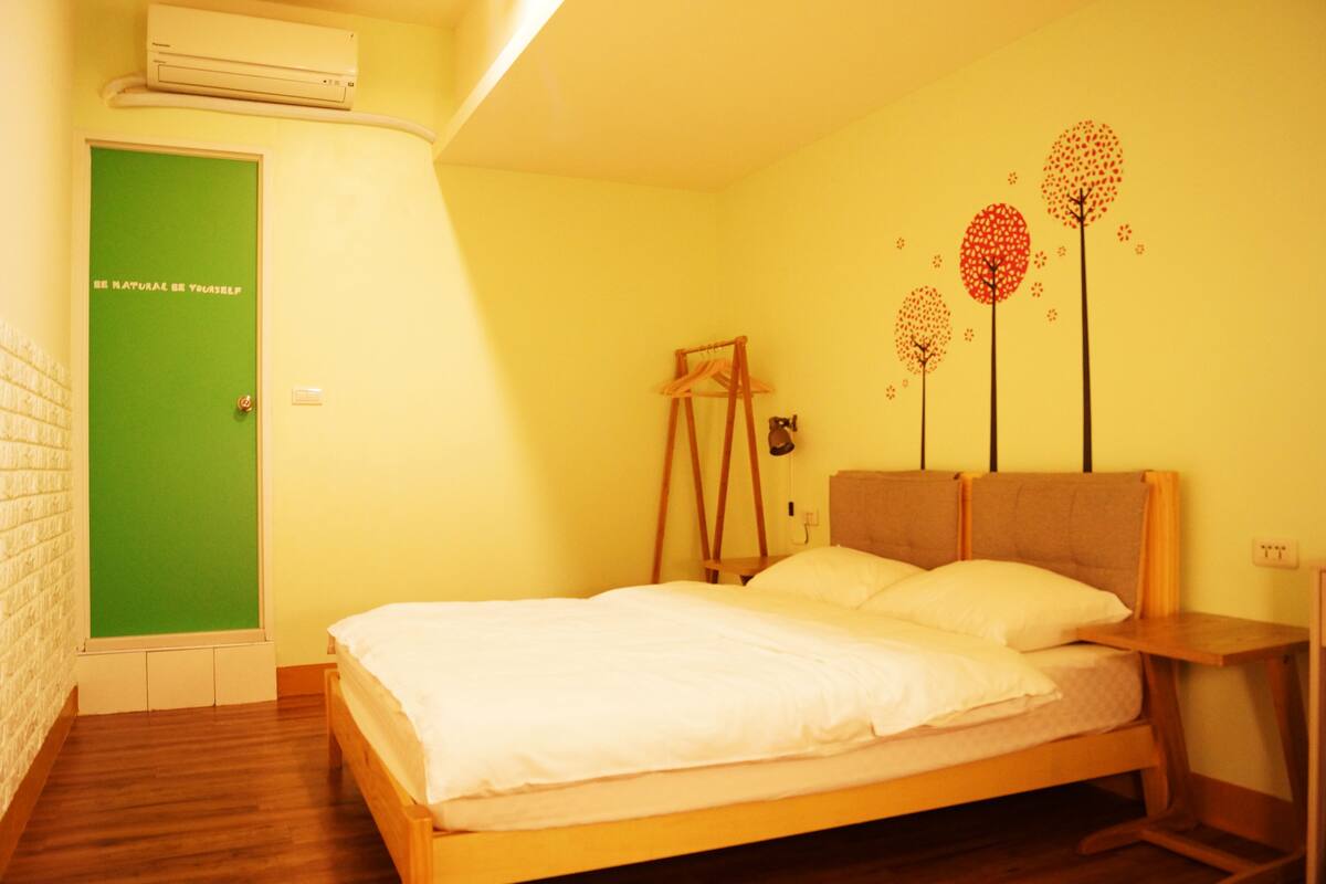 A room with a bed, a green door, and a wall with tree decorations.