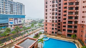 A high-rise building with a swimming pool, surrounded by palm trees and a busy street. - Marina Travellers Suite Marina Court (Kota Kinabalu)