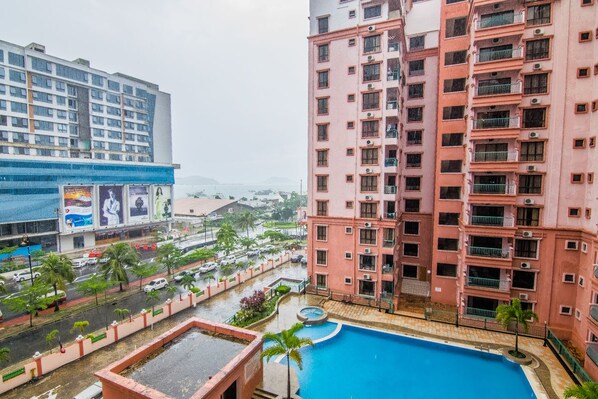 A high-rise building with a swimming pool, surrounded by palm trees and a busy street.