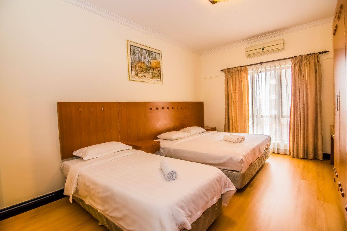 A hotel room with two single beds, a wooden headboard, a painting on the wall, and a window with curtains.