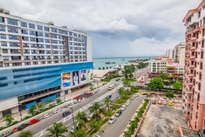 A multi-story hotel with a large billboard, a busy street with cars, and a view of the sea. - Marina Travellers Suite Marina Court (Kota Kinabalu)