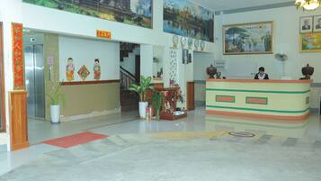 A hotel lobby with a reception desk, a staircase, and a large painting on the wall.