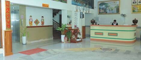 A hotel lobby with a reception desk, a staircase, and a large painting on the wall.
