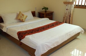 A neatly made bed with white linens and a red patterned throw, a bedside table with a plant, and a window with curtains. - Lux Star Town Hotel (Phnom Penh)