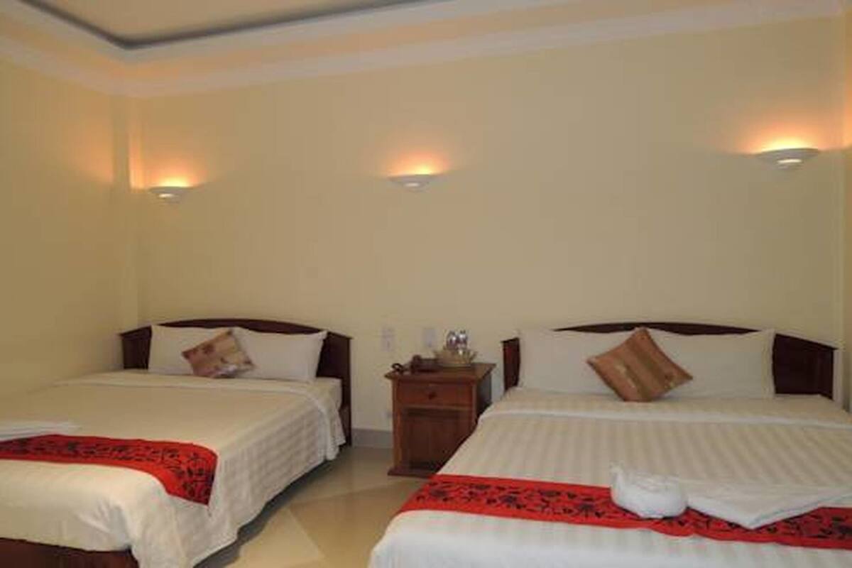 Habitación de hotel con dos camas, cada una con cabecero de madera, una mesita de noche entre ellas y una lámpara fijada a la pared sobre cada cama.