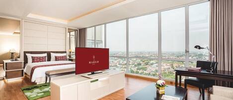 A modern hotel room with a large bed, a TV, a desk, and a view of the city.