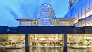 Un edificio moderno con una llamativa estructura de cúpula de cristal, un vestíbulo amplio con zonas de estar y una escalera visible que conduce a los pisos superiores.