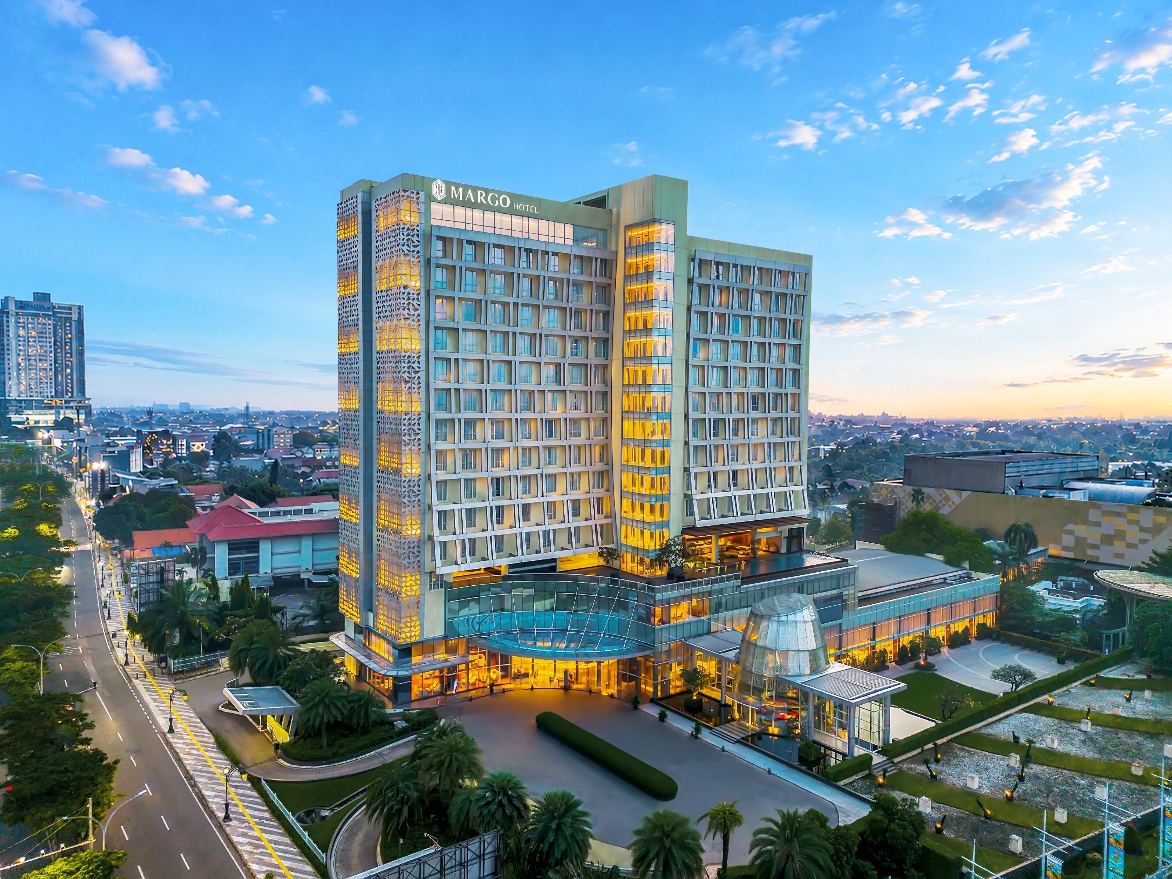 A modern hotel with a prominent entrance, a rooftop pool, and a surrounding landscaped area.