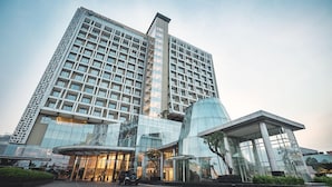 Un hotel moderno con una estructura alta y rectangular, amplias ventanas de vidrio y una entrada de vidrio con forma curva.