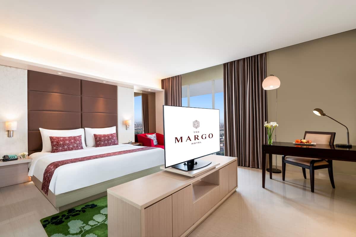 A hotel room with a bed, a desk, a television, and a view of the city.