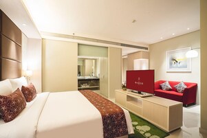Quarto de hotel com uma cama, sofá vermelho, televisão e espelho.