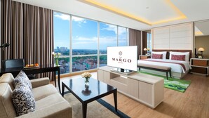 Una habitación de hotel moderna con una cama grande, televisión, sofá, una mesa de centro y vistas de la ciudad.
