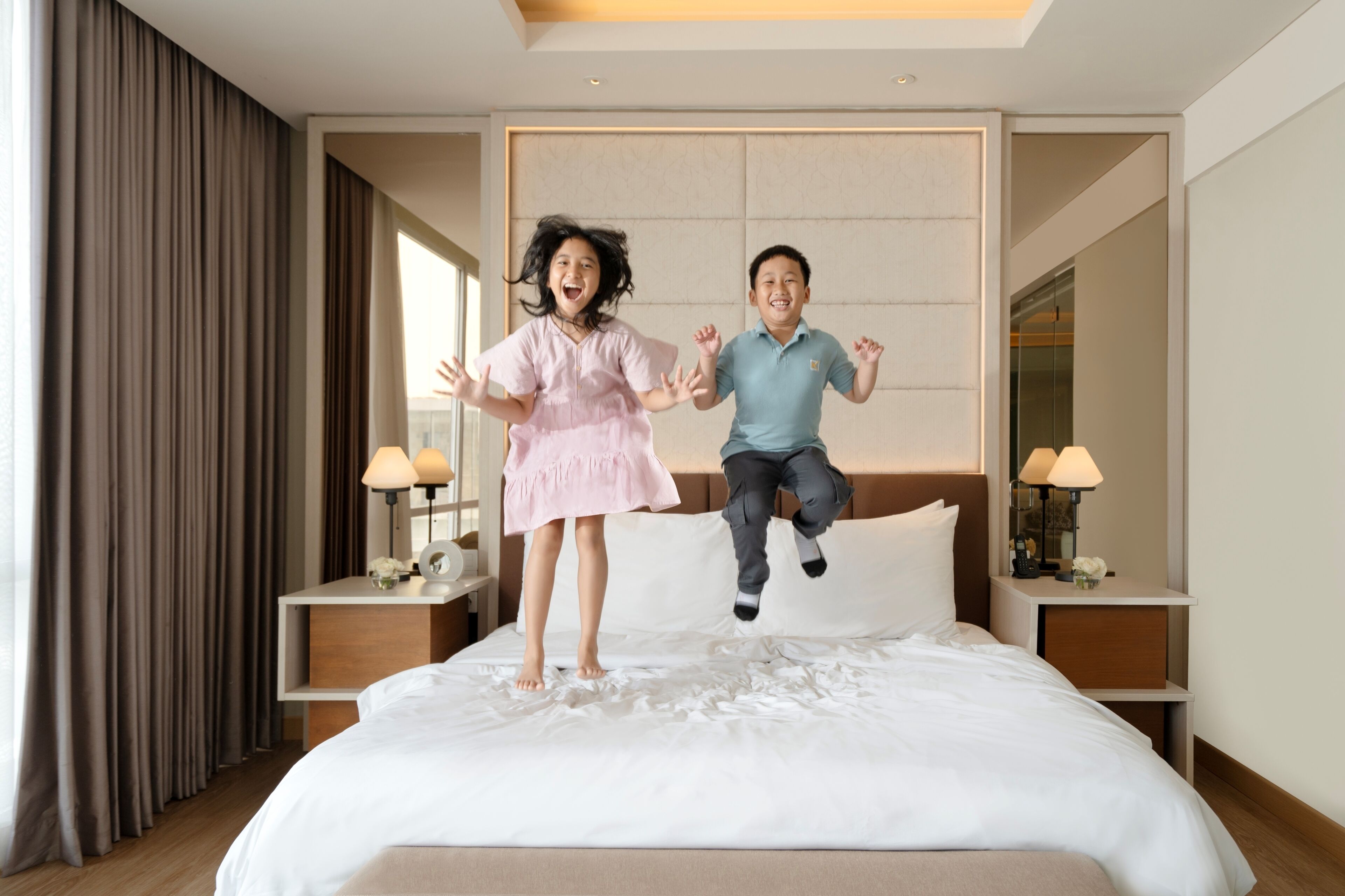 A hotel room with a bed, nightstands, lamps, and a large window with curtains.