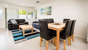 A modern living room with a dining area, featuring a sofa, a coffee table, and a dining table with chairs.
