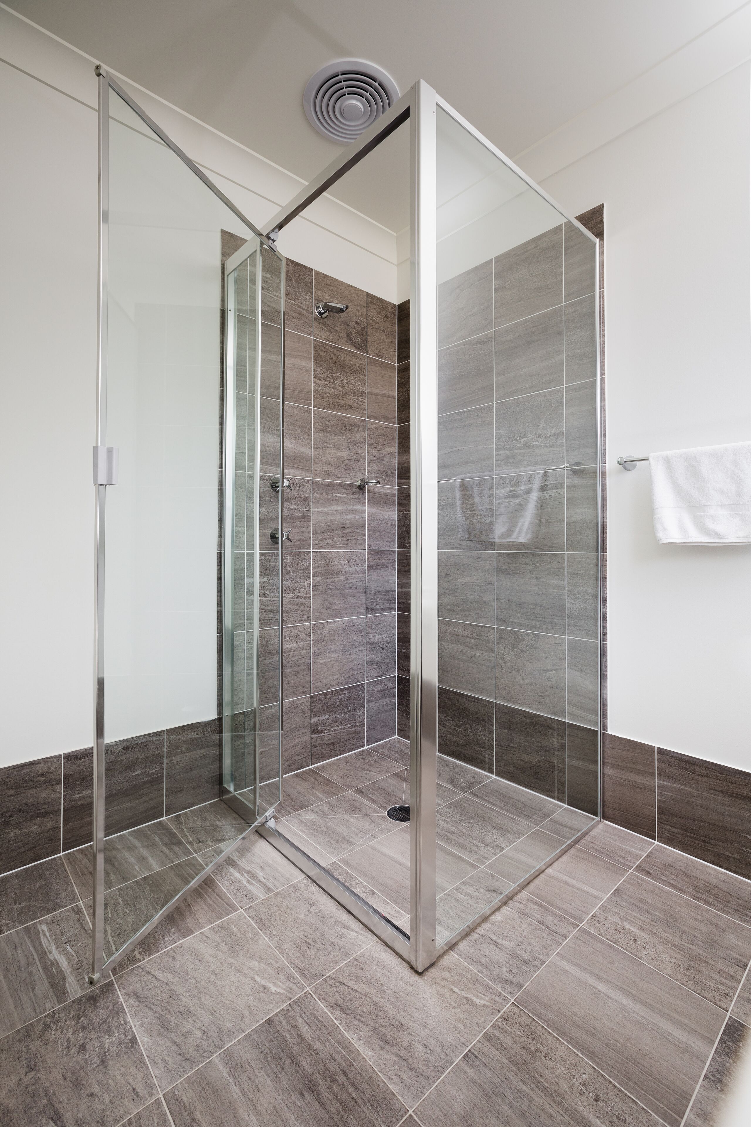 Un baño moderno con ducha envuelta en vidrio, paredes con azulejos y una toalla blanca colgada en la pared.