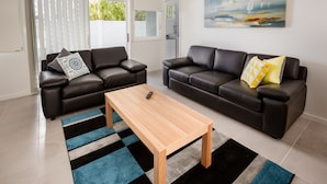A modern living room with two black leather sofas, a wooden coffee table, and a colorful striped rug.