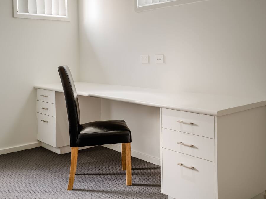 Un escritorio blanco con una silla negra, un cajón y un archivador pequeño.