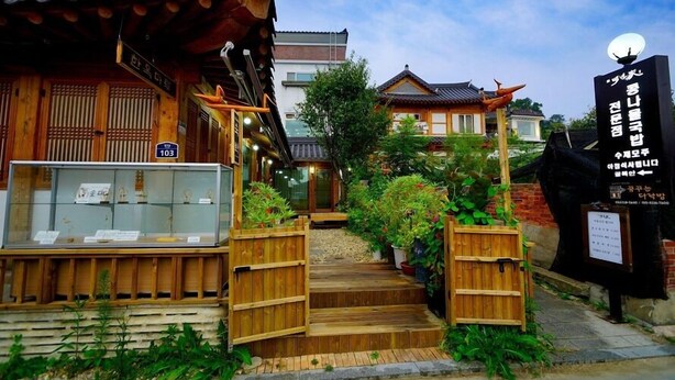 A traditional Korean wooden building with a wooden gate, a display case with items, and a signboard.