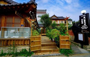 A traditional Korean wooden building with a wooden gate, a display case with items, and a signboard. - Hanokmaru (Jeonju)