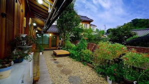 A traditional Japanese-style garden with a wooden walkway, potted plants, and a small wooden bench.