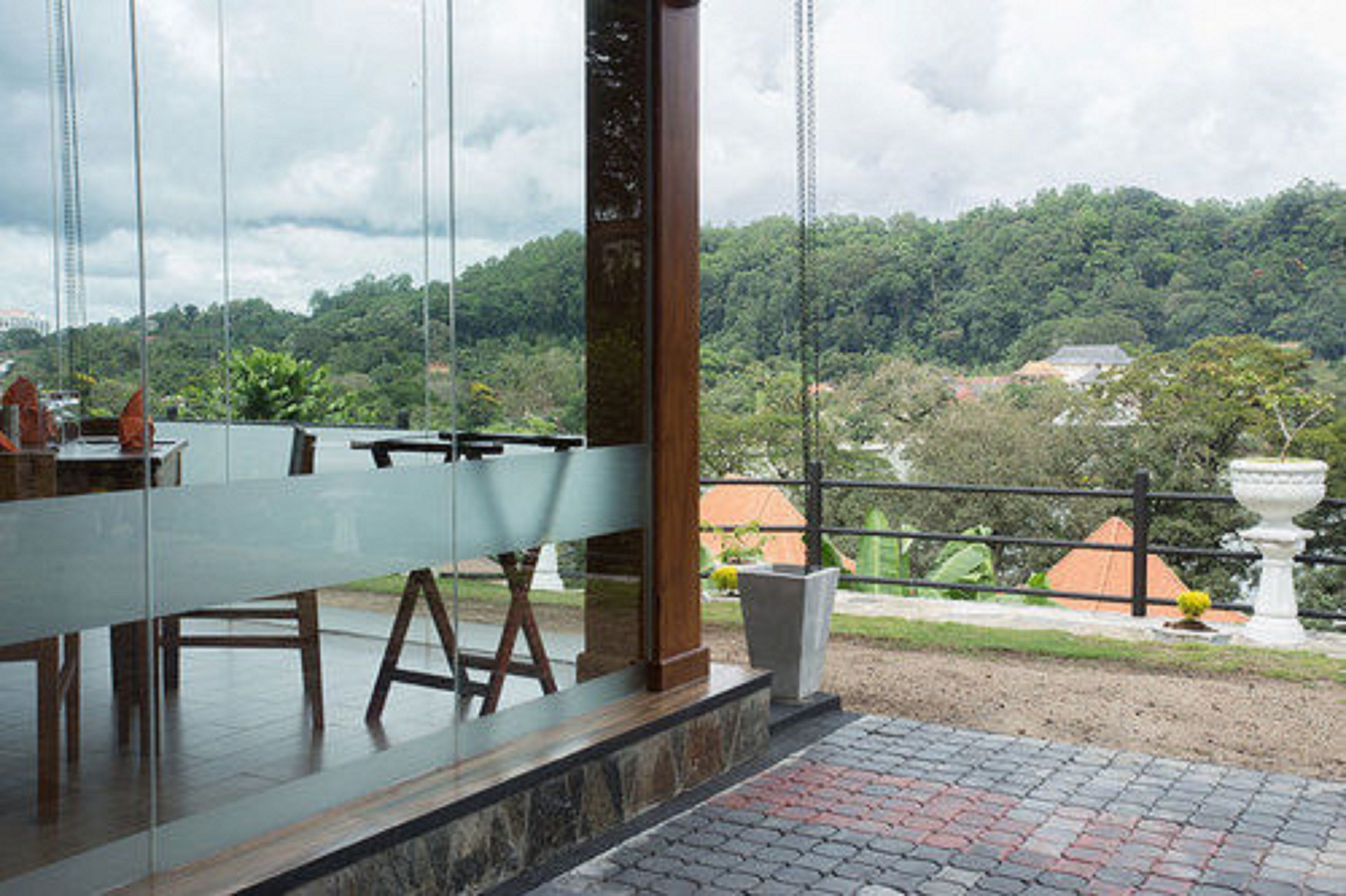 A modern restaurant with a glass enclosure, offering views of a lush green landscape and distant buildings.