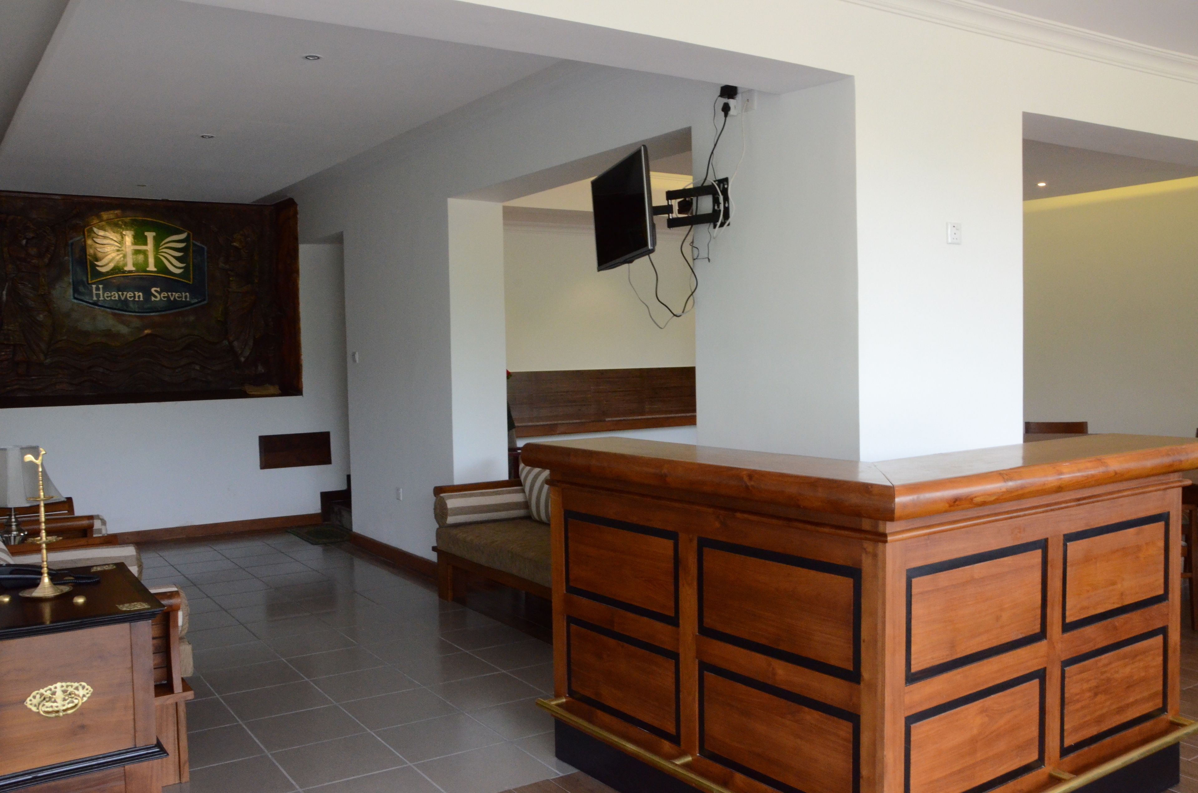 A reception area with a wooden reception desk, a flat-screen TV mounted on the wall, a sofa, and a sign with a logo.
