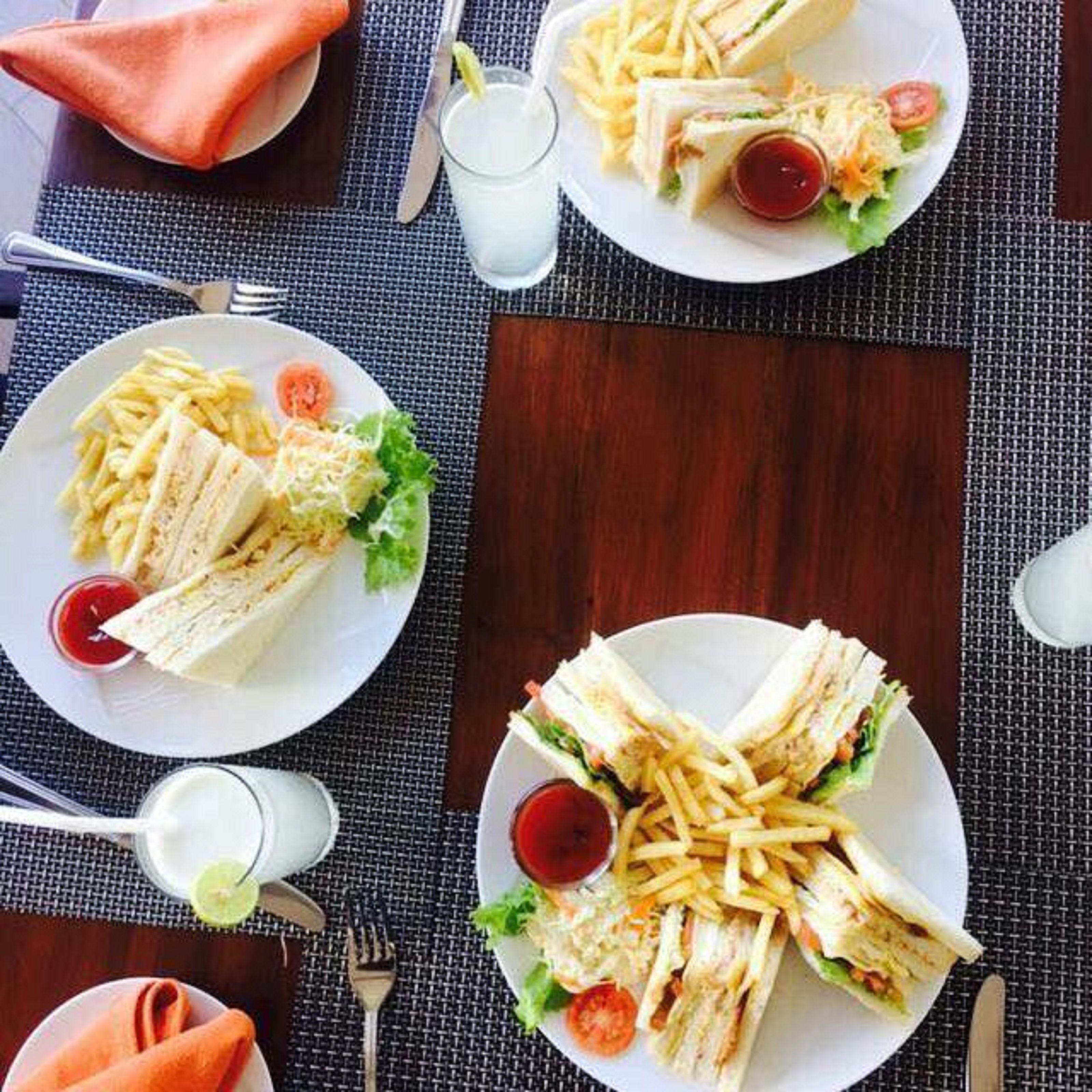 A table set with plates of sandwiches, fries, and salad, accompanied by condiments and drinks.