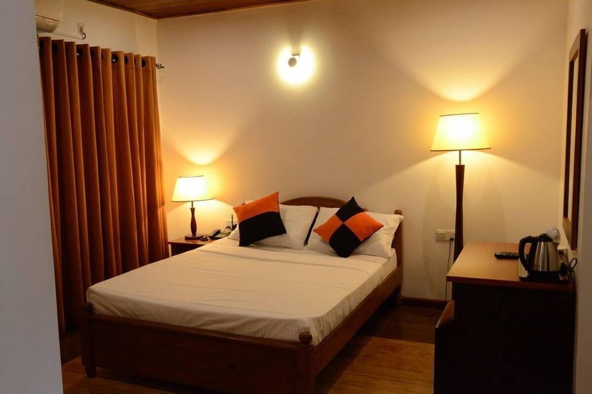 A hotel room with a bed, two bedside lamps, a nightstand, a wooden desk, and a curtain.