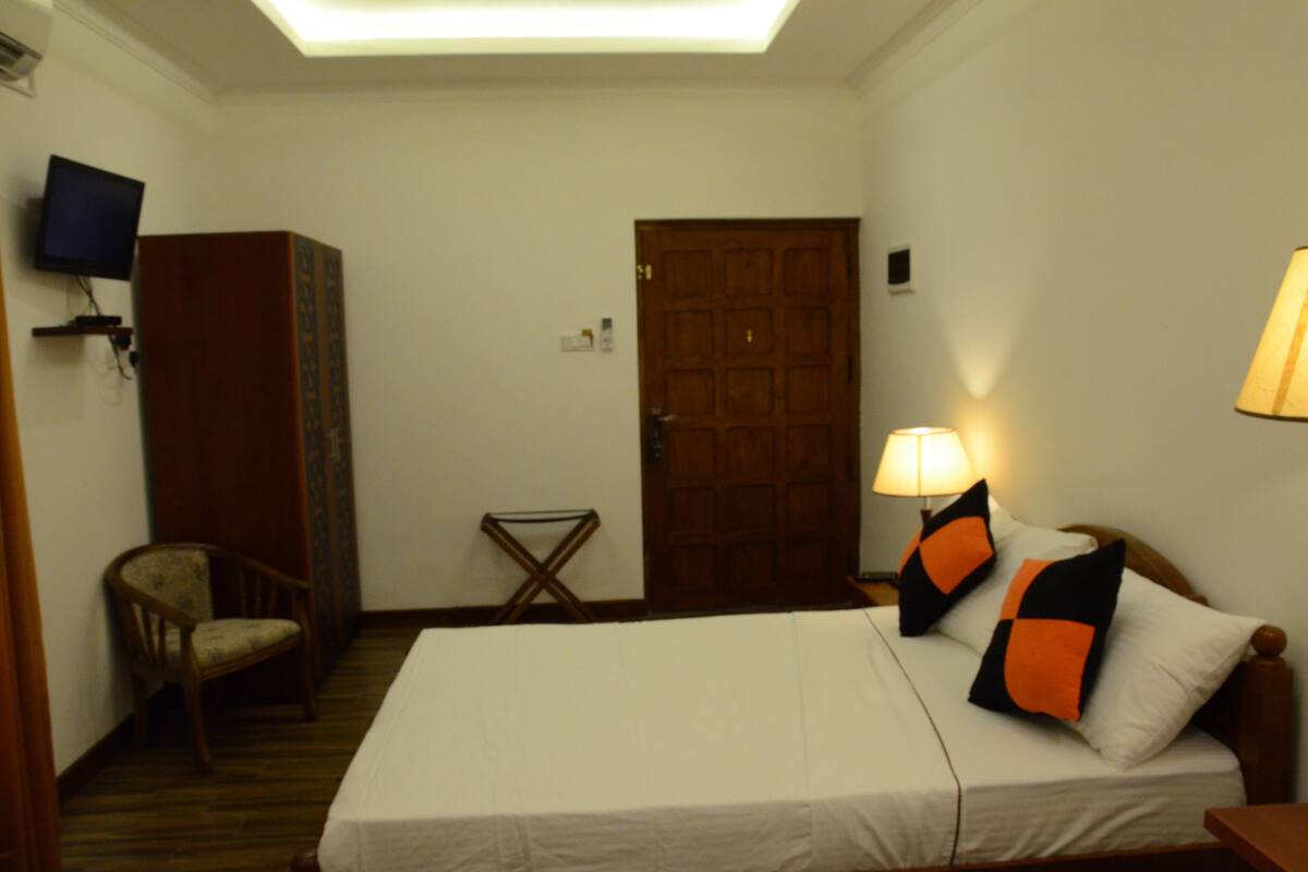 A hotel room with a bed, a chair, a television, a wooden door, and a lamp.