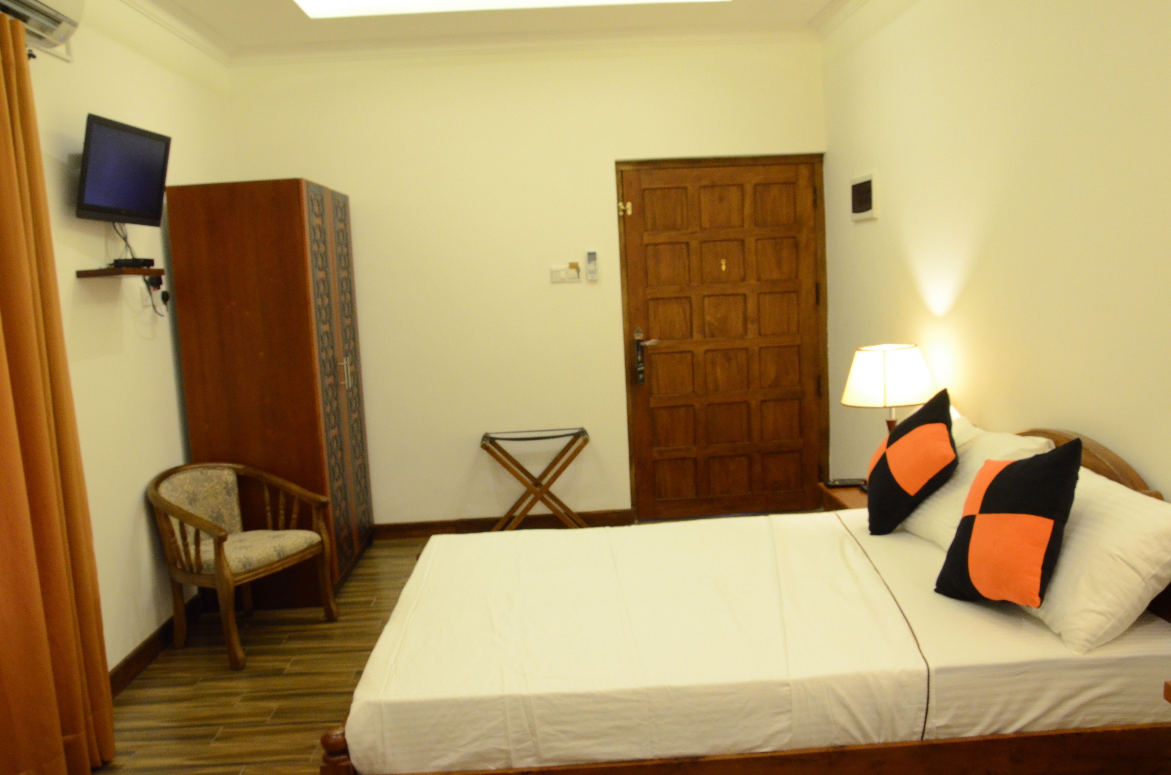 A hotel room with a bed, a chair, a television, and a wooden door.