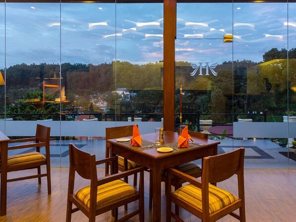 Un comedor con una mesa dispuesta para cuatro, rodeada de sillas de madera con cojines amarillos, ventanas amplias que ofrecen vistas a un paisaje boscoso y un diseño de techo moderno.