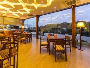 Een restaurant met houten meubels, grote ramen en uitzicht op de stad.
