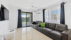 A modern living room with a leather sofa, a TV mounted on the wall, and a sliding glass door leading to an outdoor area. - Casa Nostra Motel (Parkhurst)