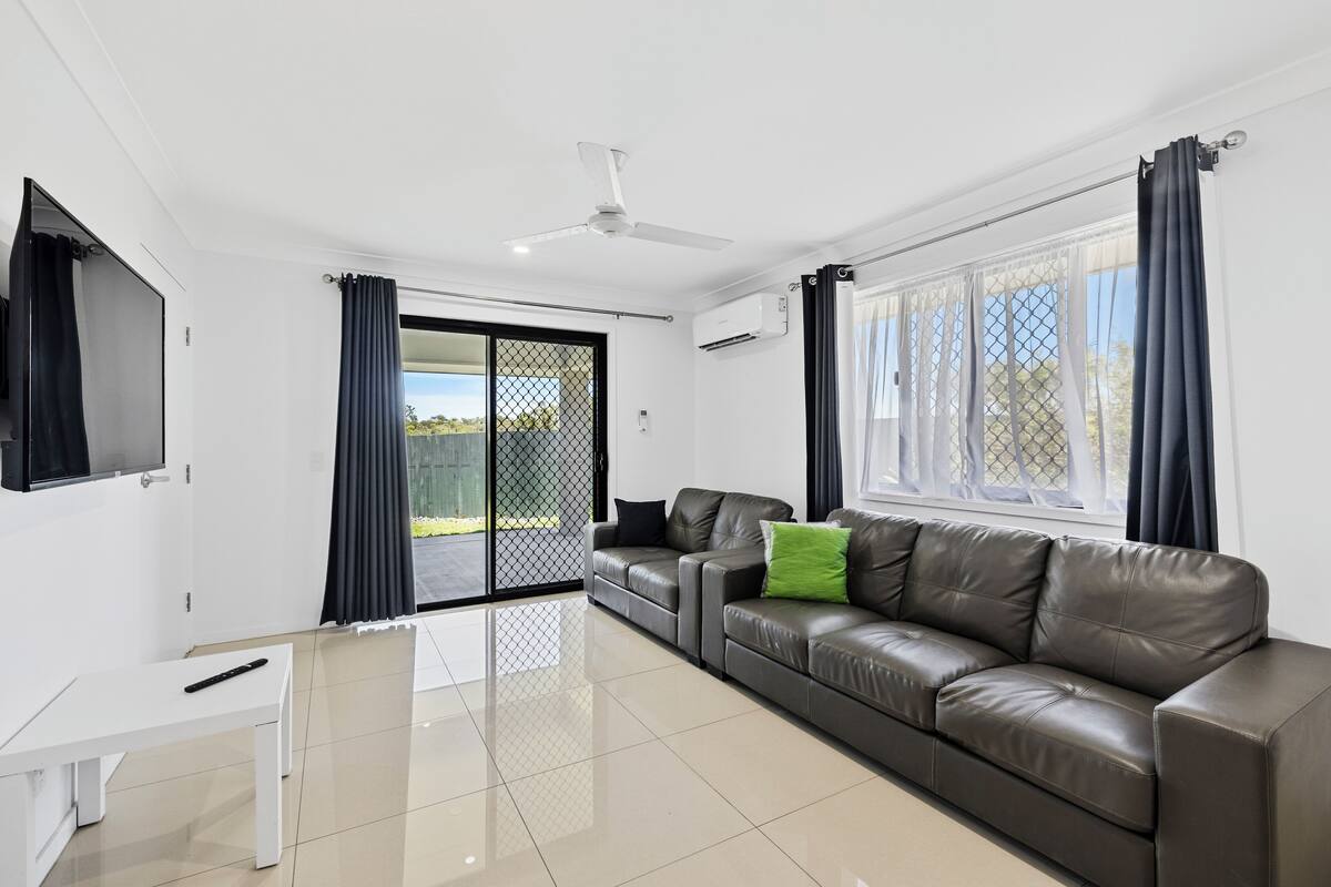 A modern living room with a leather sofa, a TV mounted on the wall, and a sliding glass door leading to an outdoor area.
