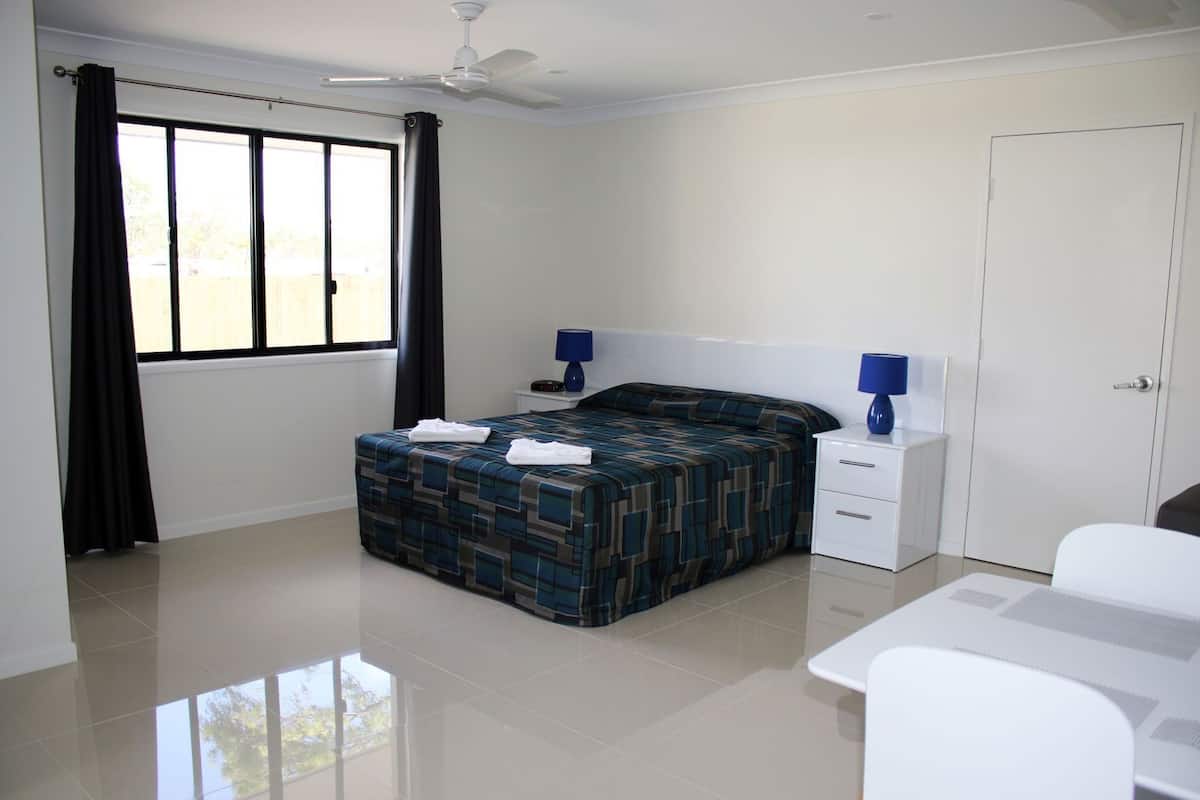 A bedroom with a bed, a nightstand, a desk, a ceiling fan, and a window with curtains.