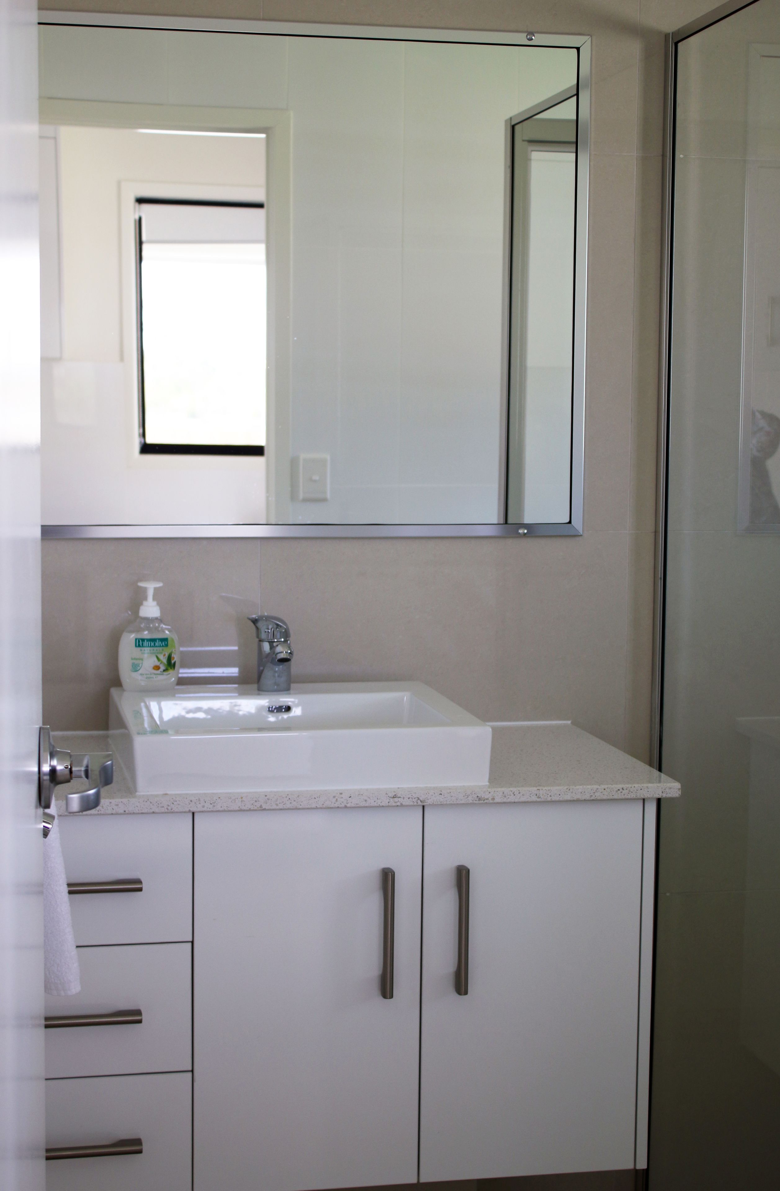 A bathroom with a white sink, a mirror, and a bottle of hand soap.
