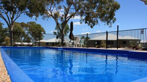 A swimming pool with a blue edge, surrounded by a black fence, and trees in the background. - Casa Nostra Motel (Parkhurst)