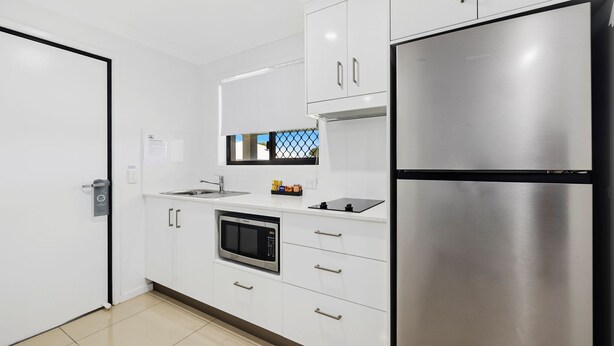 A modern kitchen with white cabinetry, a stainless steel refrigerator, a microwave, and a sink. - Casa Nostra Motel (Parkhurst)