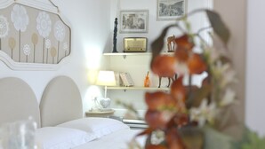Ett välordnat sovrum med en säng, ett sängbord, en lampa och dekorativa föremål, inklusive en radio och inramade bilder.