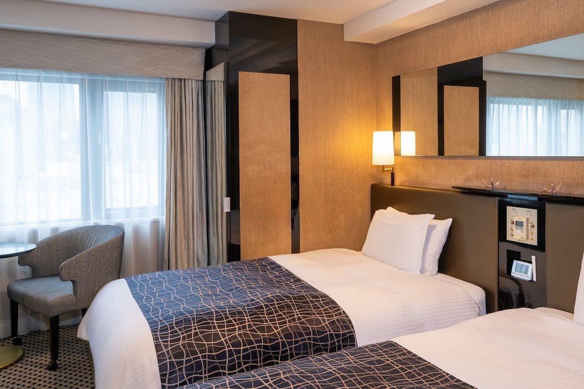 Ett hotellrum med två sängar, ett skrivbord, en stol, en stor spegel och ett fönster med gardiner.