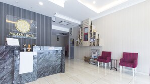 A hotel reception area with a marble counter, two red upholstered chairs, a small table, and a wall-mounted trophy display. - Palazzo Hotel Kulai (Kulai)
