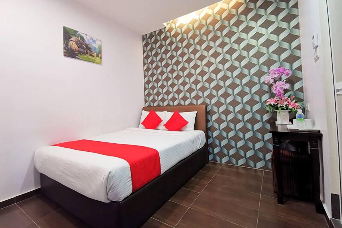 Een hotelkamer met een bed, een nachtkastje, een muur met een geometrisch patroon en een kleine tafel met een bloevas.