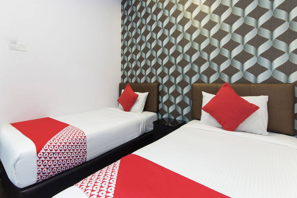 Een hotelkamer met twee bedden, elk met een sprei met een rood-wit patroon. De muren zijn voorzien van behang met een geometrisch patroon.