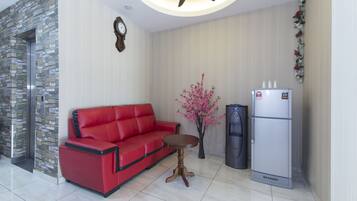 A modern living room with a red sofa, a small wooden table, a decorative plant, a refrigerator, and a stone wall.