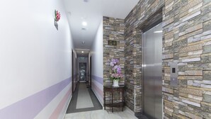A hallway with a stone wall, an elevator, and a door at the end. - Palazzo Hotel Kulai (Kulai)