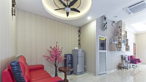 A modern living room with a red sofa, a small wooden table, a decorative tree, a refrigerator, and a ceiling fan. - Palazzo Hotel Kulai (Kulai)