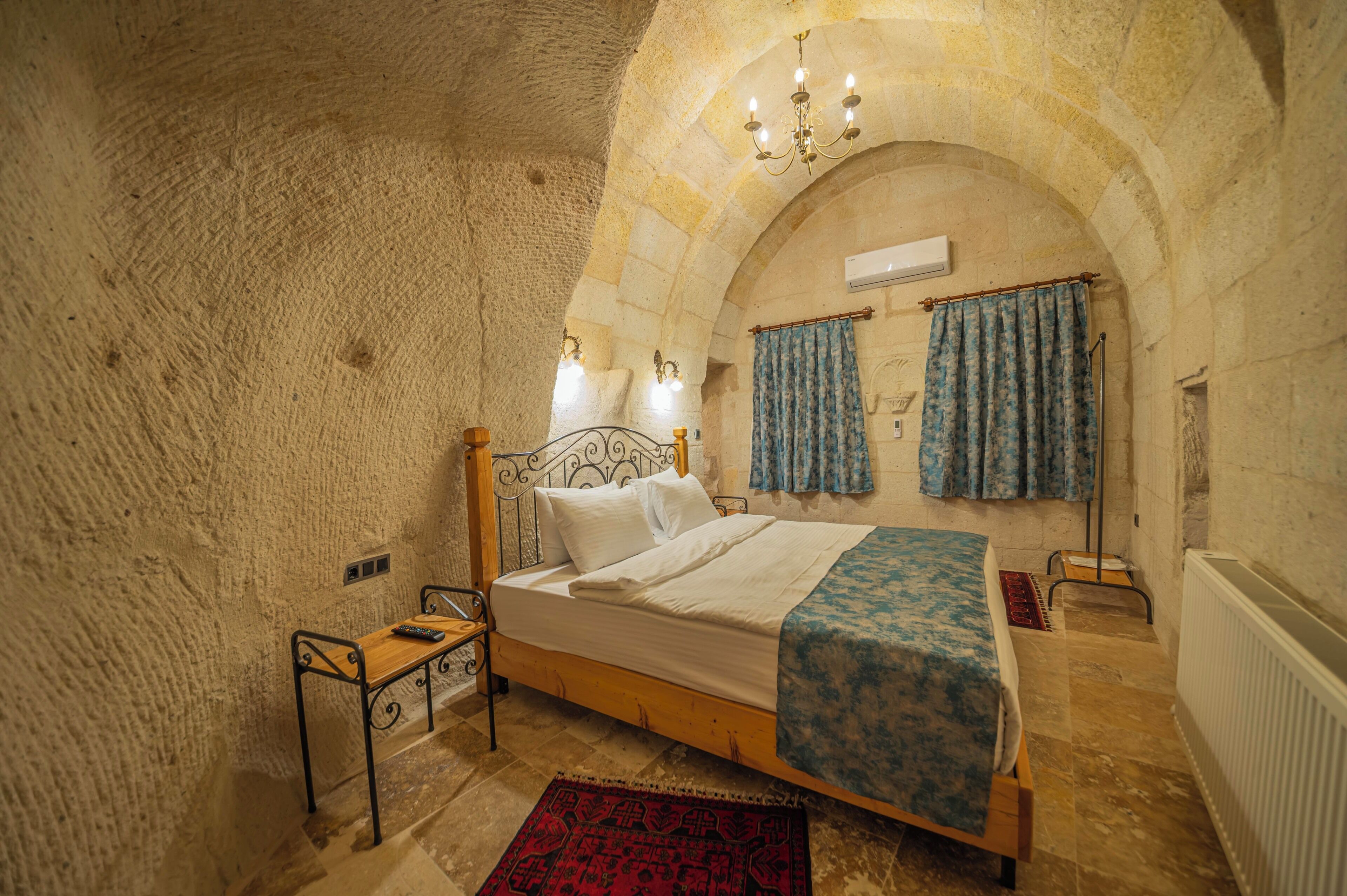 Ein Schlafzimmer mit Steinwand, einem hölzernen Bett, einem Nachttisch, einem roten Teppich und einer Kronleuchter.